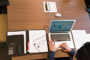 Overhead view of a person working remotely with a laptop and documents on a wooden desk.